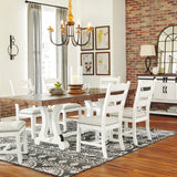 A dining room scene showing a white wooden dining table with six matching ladder-back chairs arranged on a patterned rug. The room has exposed brick walls, hardwood floors, a chandelier, framed wall art, and a white sideboard cabinet with lamps.