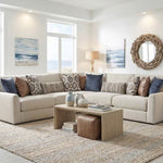 A beige sectional sofa with multiple throw pillows in blue, brown, and patterned designs, styled in a bright, modern living room with a wooden coffee table and a large woven rug.