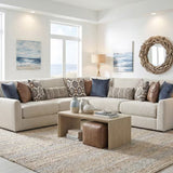 A beige sectional sofa with multiple throw pillows in blue, brown, and patterned designs, styled in a bright, modern living room with a wooden coffee table and a large woven rug.