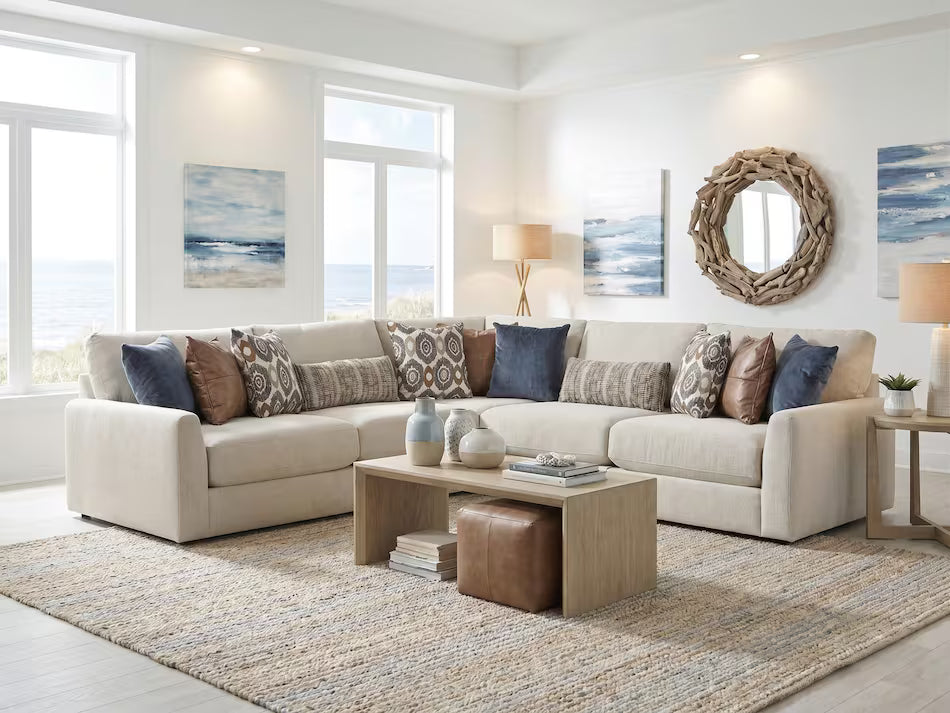 A beige sectional sofa with multiple throw pillows in blue, brown, and patterned designs, styled in a bright, modern living room with a wooden coffee table and a large woven rug.
