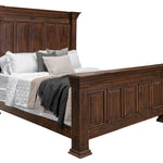 A dark brown wooden bed frame with a tall paneled headboard and matching footboard, shown with white bedding, gray pillows, and a dark throw blanket on a plain white background.