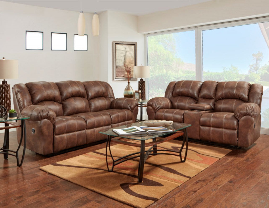 Brown leather reclining sofa and matching loveseat in a bright living room with wood floors, a glass-top coffee table, and a patterned area rug.