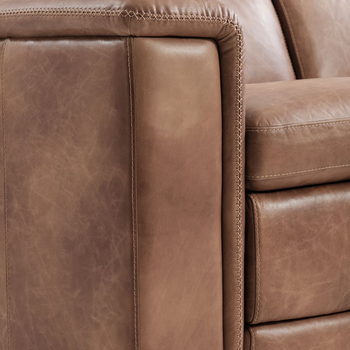 Close-up of a brown leather reclining sofa showing the armrest, seat cushion, and decorative stitching.