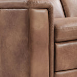 Close-up of a brown leather reclining sofa showing the armrest, seat cushion, and decorative stitching.