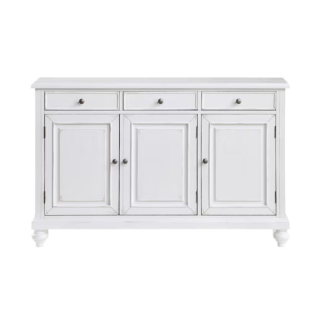 A white wooden sideboard cabinet with three drawers on top and three paneled doors below, featuring small round silver knobs and turned feet, shown against a plain white background.