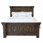 A dark brown wooden bed frame with a tall paneled headboard and matching footboard, styled with white bedding and pillows against a plain white background.