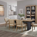 Modern dining room with wooden table and chairs, bookshelf, and kitchen in the background.