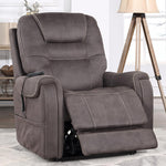 A gray-brown power recliner chair with a footrest extended, shown in a styled living room setting with a tripod floor lamp, shelving, and a window.