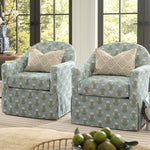 Two matching upholstered armchairs with a light blue floral pattern and beige patterned throw pillows, set in a bright living room in front of large windows.