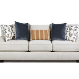 A three-seat upholstered sofa in a light warm gray or off-white fabric, styled with five decorative throw pillows including two navy blue velvet pillows, two patterned white pillows, and one tan striped pillow, shown against a plain white background.