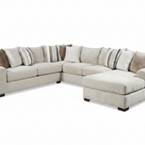 A light beige fabric sectional sofa with a chaise lounge on the right side, styled with multiple throw pillows in neutral tones, set against a plain white background.