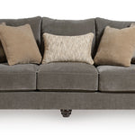 A three-seater upholstered sofa in dark gray fabric, styled with five throw pillows including two plaid and two solid beige/cream cushions, shown against a plain white background.