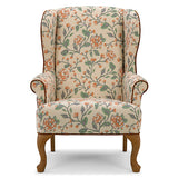A classic wingback armchair upholstered in a beige fabric with a detailed floral vine pattern in orange and green, featuring dark brown wooden legs and trim.