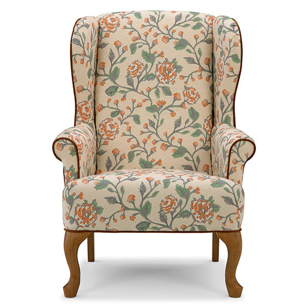A classic wingback armchair upholstered in a beige fabric with a detailed floral vine pattern in orange and green, featuring dark brown wooden legs and trim.