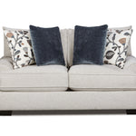 A light beige upholstered loveseat with two dark navy velvet throw pillows and two patterned accent pillows, shown against a plain white background.