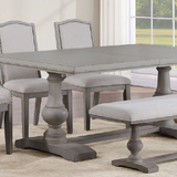 A 7-piece dining room set featuring a gray wood-topped table with turned pedestal legs, four light gray upholstered chairs with nailhead trim, and a matching upholstered bench, shown in a bright dining room setting.
