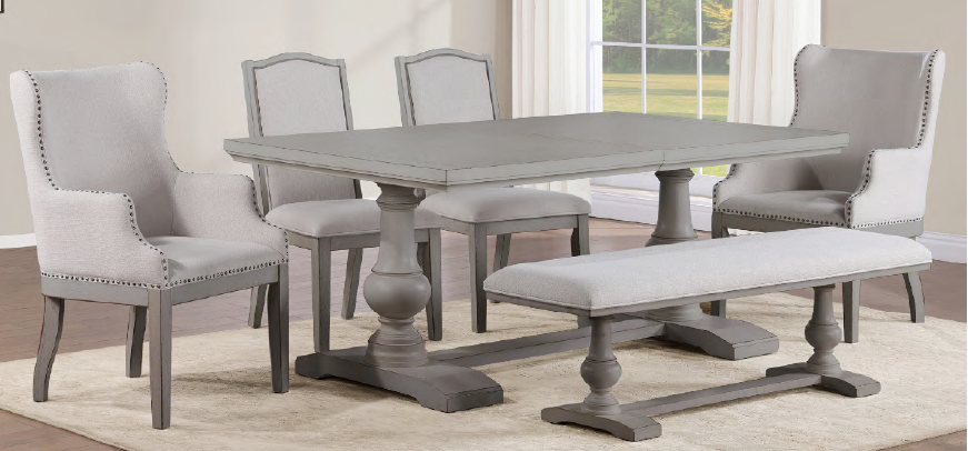 A 7-piece dining room set featuring a gray wood-topped table with turned pedestal legs, four light gray upholstered chairs with nailhead trim, and a matching upholstered bench, shown in a bright dining room setting.