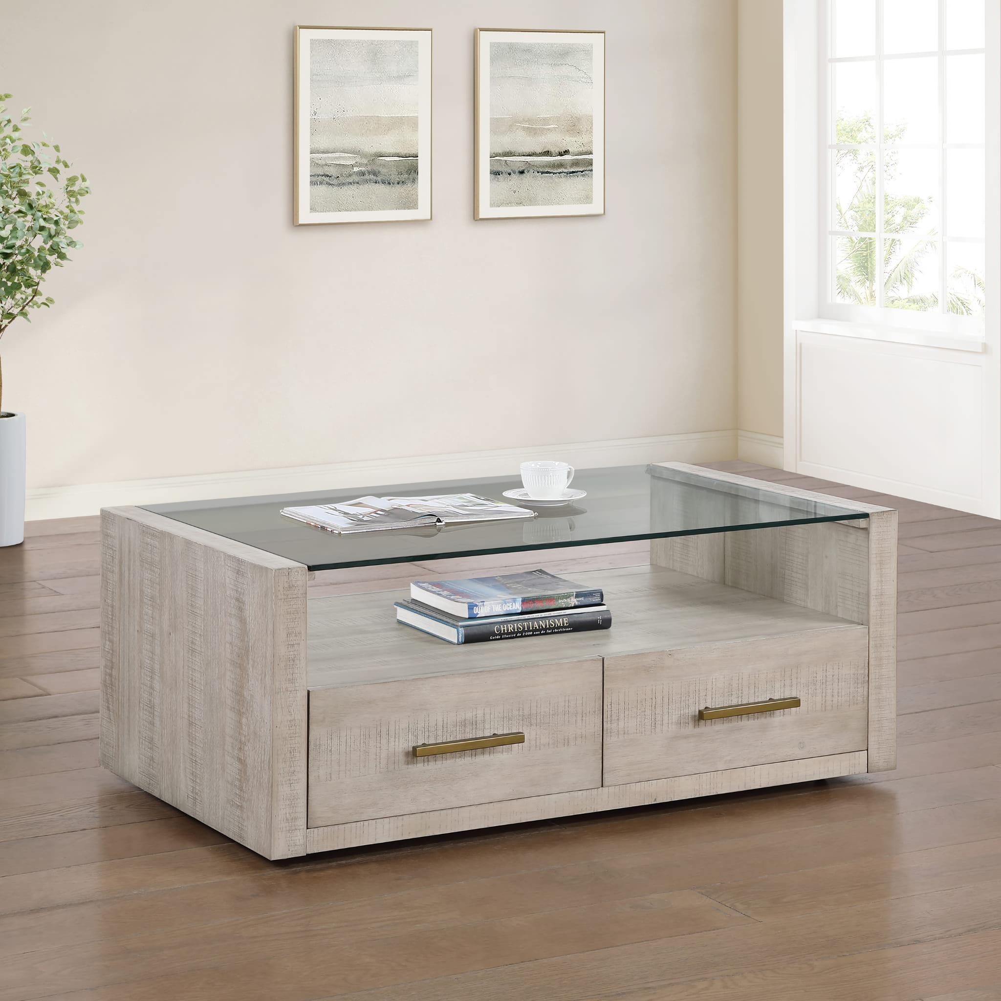 Coffee or cocktail table with a glass top and a wooden base in a room with framed pictures on the wall.
