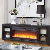 A modern dark gray electric fireplace TV stand console with a glowing orange and yellow flame effect, styled in a living room setting.