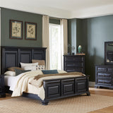 A 7-piece bedroom furniture set in a dark charcoal gray finish, including a bed frame with a paneled headboard, a nightstand, a dresser, a chest, and a matching mirror, styled in a modern bedroom with dark gray walls and beige curtains.