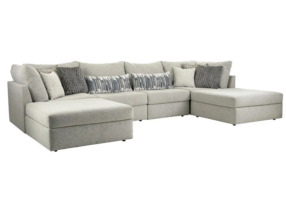 A light gray fabric sectional sofa with a chaise lounge on the left and a right-facing chaise, styled with multiple throw pillows including gray and patterned accent pillows, shown against a plain white background.