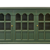 A green wooden cabinet with six glass-paneled doors arranged in three pairs of three arched windows each, featuring small brass knobs, shown against a plain white background.