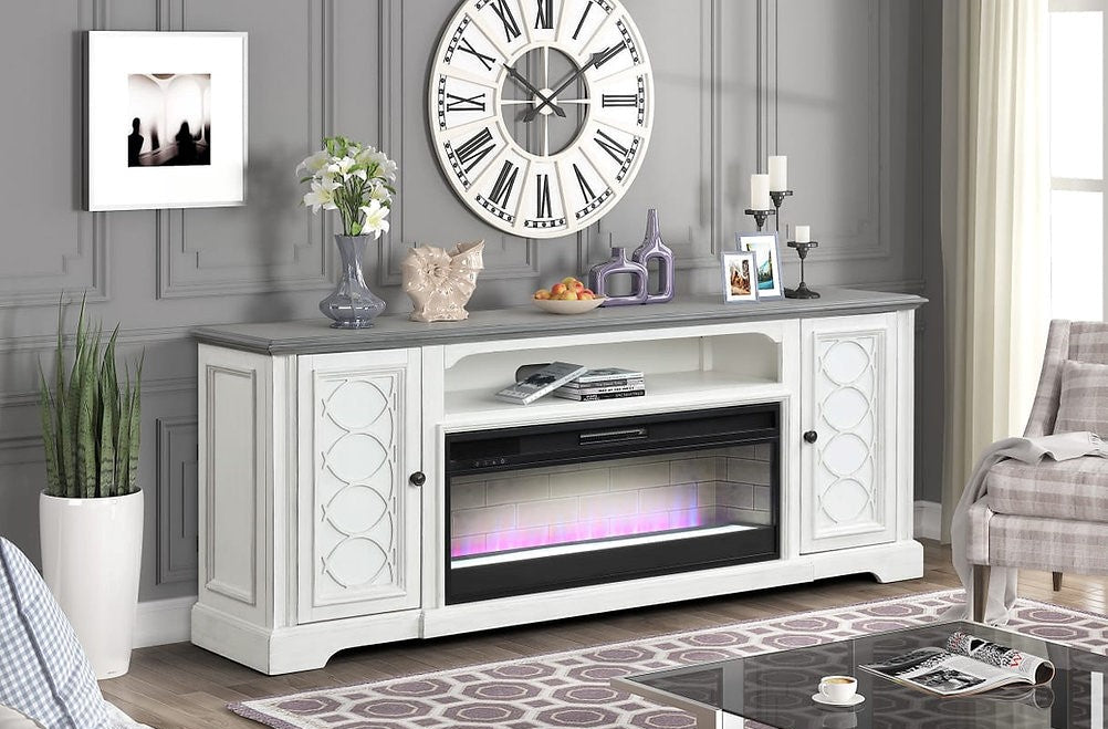 A white electric fireplace TV stand console with a gray stone-look top, styled in a modern living room setting with a patterned rug, coffee table, and wall clock.